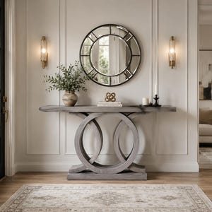 May include: A gray wooden console table with a circular base, topped with a round mirror and decorative items. Two sconces flank the mirror. A vase of greenery and a patterned rug complete the entryway decor.