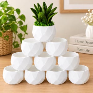 May include: A stack of ten white ceramic planters with a geometric faceted surface. The top planter holds a green succulent plant. Each planter has a rounded shape with a wide opening and a smooth matte finish, arranged in a pyramid formation.