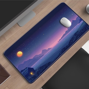 Op de afbeelding: Een rechthoekige muismat met een digitaal kunstlandschap met een zonsondergang, bergen en een klein huis met een verlicht raam. Een witte computermuis ligt op de mat. Een bruin notitieboek en een kopje koffie zijn ook zichtbaar.