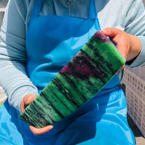 May include: A large, wedge-shaped polished mineral specimen featuring a vibrant green base color with prominent black streaks and deep magenta-colored inclusions throughout the stone, displaying a smooth, glossy surface texture.
