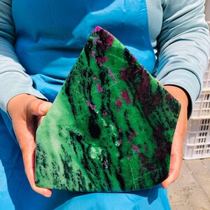 May include: A large, polished, triangular-shaped slab of zoisite mineral featuring a vibrant green base color with prominent, irregular black hornblende streaks and scattered, deep magenta-colored ruby inclusions throughout the stone surface.