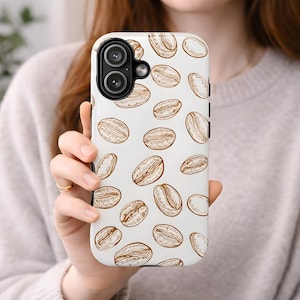 May include: A white phone case with a repeating pattern of brown coffee bean illustrations. The case has a camera cutout and side buttons. The phone case is held by a person.