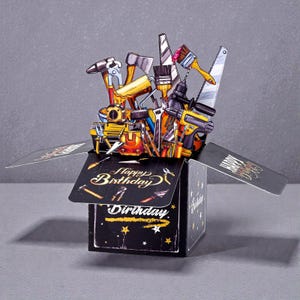 May include: A pop-up birthday card with a selection of tools in yellow, black, and silver. The card is black with gold stars and the words "Happy Birthday" and "Birthday" in gold script.