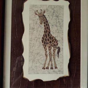 May include: Framed artwork featuring a giraffe illustration. The giraffe has brown spots and is set against a textured, off-white background. The artwork is framed with a brown, textured border and a white mat, encased in a dark wooden frame.