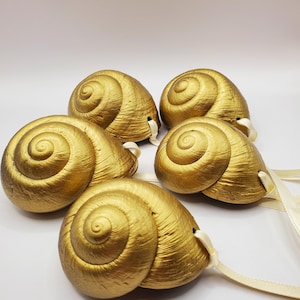 May include: Five gold snail shell ornaments with white ribbon loops. The shells are shiny and have a textured surface.