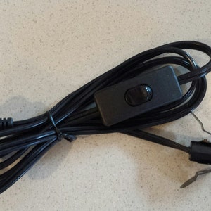 May include: Black electrical cord with a black inline switch and a standard US plug on one end and a black lamp socket on the other end.