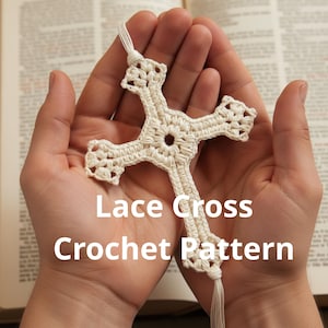 May include: A cream-colored, crocheted lace cross with the text "Lace Cross Crochet Pattern". The cross is held in open hands against a blurred background of a book. The cross has a detailed, openwork design.