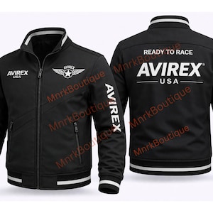 K&ouml;nnte beinhalten: Schwarze Bomberjacke mit wei&szlig;en Akzenten und dem Text "AVIREX USA". Die Jacke hat einen Rei&szlig;verschluss, Seitentaschen und "READY TO RACE" &uuml;ber dem Markennamen auf der R&uuml;ckseite. Der Markenname ist vertikal auf den &Auml;rmeln aufgedruckt.
