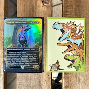May include: Two trading cards are displayed. One card features a holographic image of a dinosaur with text that reads "Gishath, Sun's Avatar." The other card has a green border and a cartoon illustration of several dinosaurs.