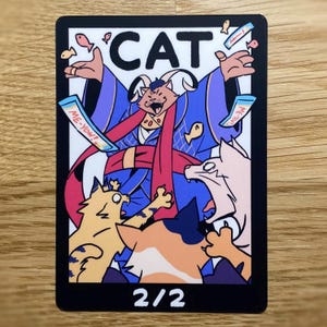 May include: A rectangular trading card featuring a central cat character in a blue robe with a red sash, surrounded by smaller cats and floating fish treats. The text CAT appears at the top, ME-YOW! on treat packages, and 2/2 at the bottom.