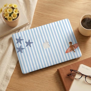 Puede incluir: Un ordenador portátil con un diseño de rayas azules y blancas, con tres estrellas de mar azules y un mono de dibujos animados surfeando en una tabla roja. El portátil está sobre una superficie de madera, con una taza de café y una maceta pequeña.
