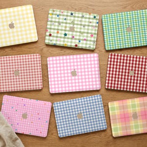 Op de afbeelding: Een collectie van negen rechthoekige laptopstickers met diverse gingham-patronen in geel, groen, rood, roze en blauw, sommige met kleine veelkleurige steraccenten, allemaal voorzien van een centrale uitsparing voor het Apple-logo.