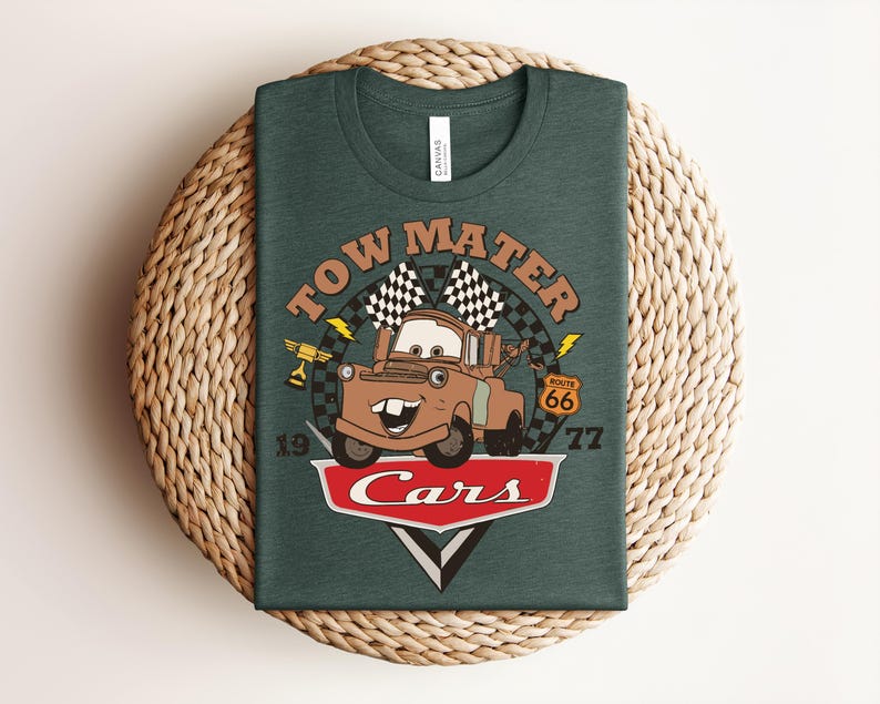 Puede incluir: Una camiseta verde oscuro con un gr&aacute;fico del personaje Tow Mater de la pel&iacute;cula Cars. El dise&ntilde;o incluye el texto Tow Mater, una bandera a cuadros, una se&ntilde;al de la Ruta 66, un trofeo y el logotipo de Cars con los n&uacute;meros 19 y 77 a los lados.