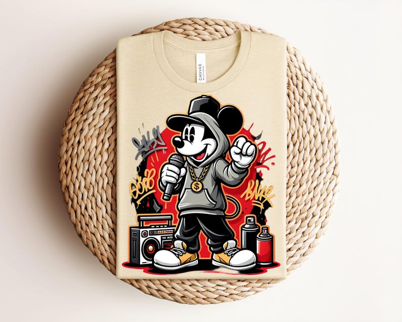 May include: Beige t-shirt featuring a cartoon Mickey Mouse in a hip-hop style. Mickey is wearing a gray hoodie, black pants, and white sneakers with yellow accents. He holds a microphone and is set against a red backdrop with graffiti art.