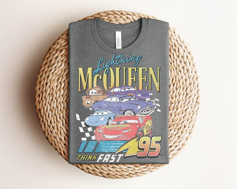 Puede incluir: Camiseta gris oscuro con un dise&ntilde;o de Rayo McQueen y otros personajes de Cars. El dise&ntilde;o incluye el texto "Lightning McQueen" en azul y amarillo, y "Think Fast" con el n&uacute;mero 95.
