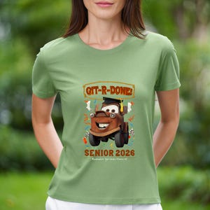 Op de afbeelding: Saliegroen T-shirt met een cartoonafbeelding van Takel uit de film Cars, met een afstudeerhoed. De tekst "GIT-R-DONE!" en "SENIOR 2026" staan erop. Het shirt heeft een ronde hals.