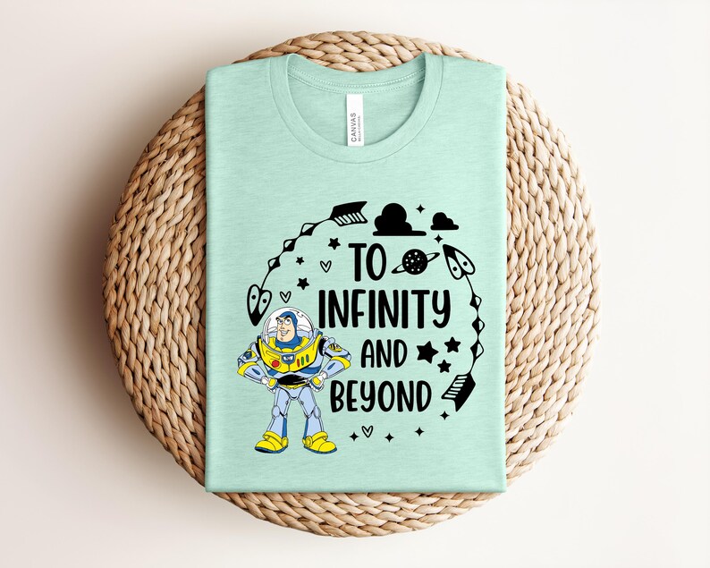 Peut inclure: Un t-shirt vert clair avec l'inscription "TO INFINITY AND BEYOND" en noir, ainsi qu'une image de dessin anim&eacute; de Buzz l'&Eacute;clair. Le design comprend des &eacute;toiles, des plan&egrave;tes et d'autres &eacute;l&eacute;ments sur le th&egrave;me de l'espace.