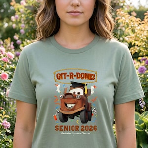 Op de afbeelding: Saliegroen t-shirt met een cartoonafbeelding van Takel uit de film Cars, met een afstudeerhoed. De tekst "GIT-R-DONE!" staat boven de afbeelding en "SENIOR 2026" eronder. Op het shirt staat ook "Radiator Springs Class of".