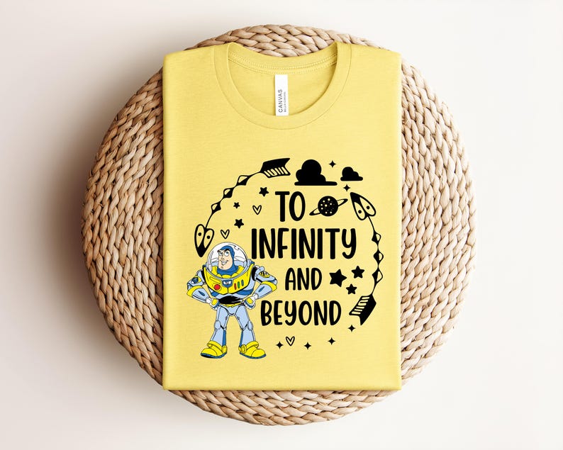 Peut inclure: T-shirt jaune avec un graphisme de Buzz l'&Eacute;clair et l'inscription "To Infinity and Beyond". Le motif comprend des &eacute;toiles, des plan&egrave;tes et des fl&egrave;ches. Le t-shirt est pli&eacute; sur un dessous de plat circulaire tiss&eacute;.