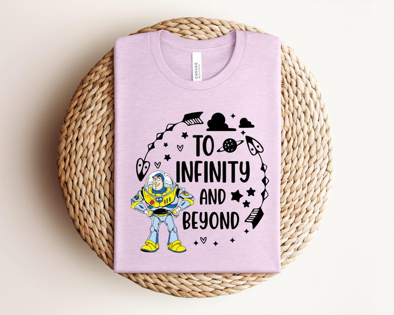 Peut inclure: Un t-shirt lilas avec un graphisme de Buzz l'&Eacute;clair et l'inscription "To Infinity and Beyond" en noir. Le motif comprend des &eacute;toiles, des plan&egrave;tes et d'autres &eacute;l&eacute;ments sur le th&egrave;me de l'espace. Le t-shirt est pli&eacute; sur un tapis tiss&eacute;.