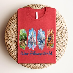 May include: A red t-shirt featuring watercolor illustrations of iconic Walt Disney World landmarks. The design includes the Tree of Life, Cinderella Castle, Spaceship Earth, and the Tower of Terror, with "Walt Disney World" in blue script.