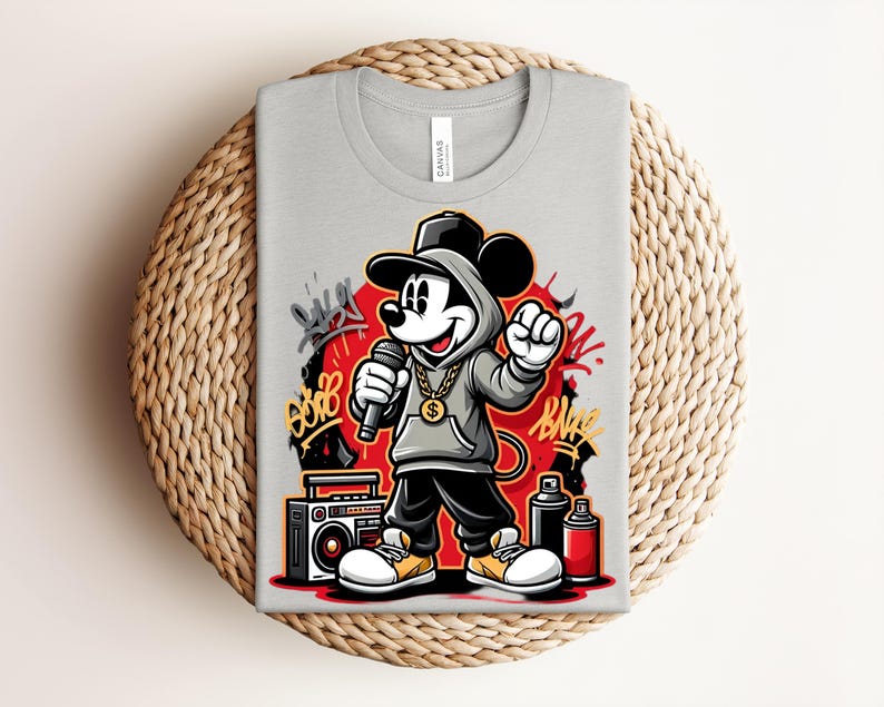 May include: A light gray t-shirt featuring a cartoon Mickey Mouse in a hip-hop style. Mickey is wearing a gray hoodie, black pants, and a gold chain, holding a microphone. Graffiti art and a boombox are also visible.