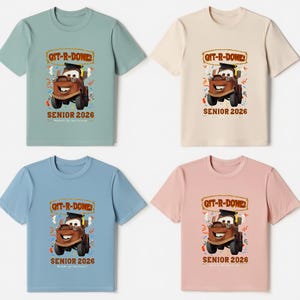 Op de afbeelding: Vier shirts met korte mouwen in verschillende kleuren: lichtgroen, beige, lichtblauw en roze. Elk shirt heeft een afbeelding van een cartoon sleepwagen met een afstudeerhoed, met de tekst "GIT-R-DONE" en "SENIOR 2026".