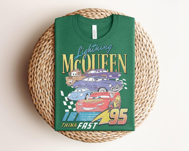 Puede incluir: Camiseta verde con un dise&ntilde;o de Rayo McQueen y otros personajes de Cars. El dise&ntilde;o incluye el texto "Lightning McQueen", "95" y "Think Fast". La camiseta est&aacute; doblada sobre una estera tejida.
