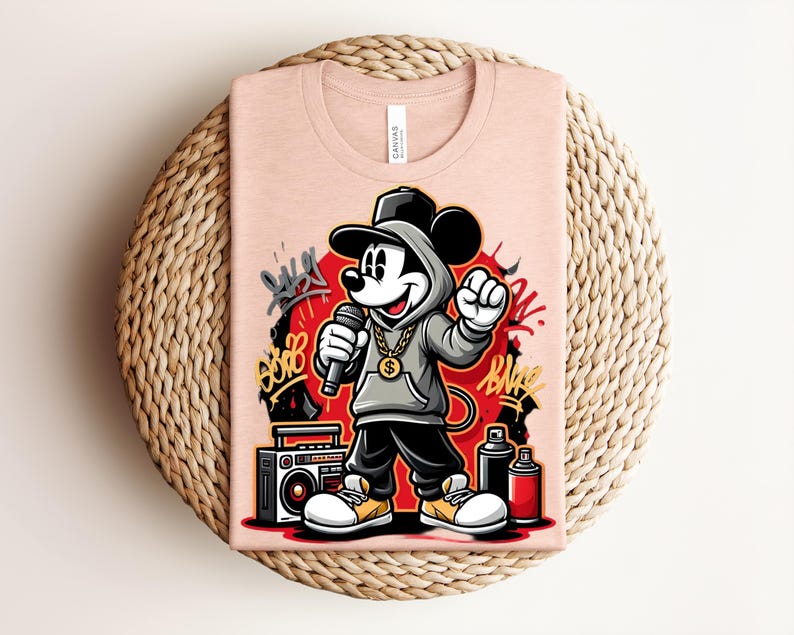 May include: A light pink t-shirt featuring a cartoon Mickey Mouse character in a hip-hop style. Mickey is wearing a gray hoodie, black pants, and a gold chain, holding a microphone. Graffiti art and a boombox are also visible.