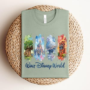 May include: Sage green t-shirt featuring watercolor illustrations of iconic Walt Disney World landmarks. The shirt includes images of the Tree of Life, Cinderella Castle, Spaceship Earth, and the Tower of Terror, with "Walt Disney World" written below.