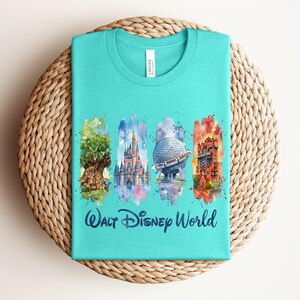 May include: A turquoise t-shirt featuring watercolor illustrations of iconic Walt Disney World landmarks. The design includes the Tree of Life, Cinderella Castle, Spaceship Earth, and Tower of Terror, with "Walt Disney World" text below.