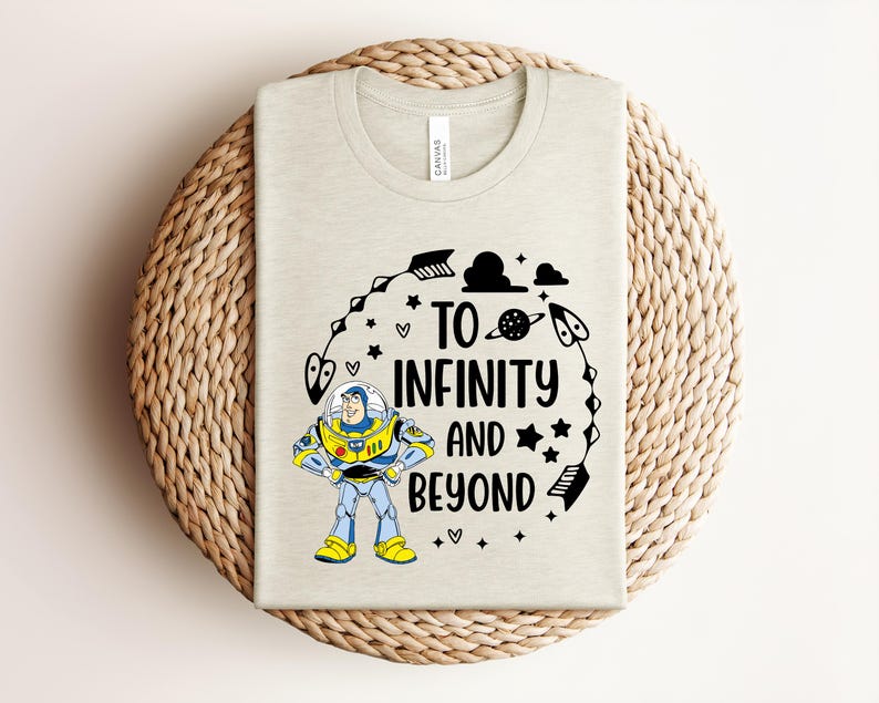 Peut inclure: Un t-shirt beige clair avec un motif de Buzz l'&Eacute;clair et l'inscription "TO INFINITY AND BEYOND" en noir. Le motif comprend des &eacute;toiles, des plan&egrave;tes et des &eacute;l&eacute;ments sur le th&egrave;me de l'espace. Le t-shirt est pr&eacute;sent&eacute; sur un tapis circulaire tiss&eacute;.