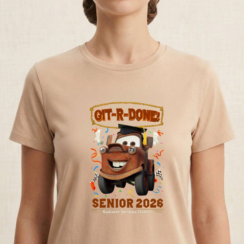 Op de afbeelding: Beige T-shirt met een cartoonafbeelding van Takel uit de film Cars, met een afstudeerhoed. De tekst "GIT-R-DONE!" staat boven de afbeelding en "SENIOR 2026" eronder. Het shirt heeft een ronde hals.