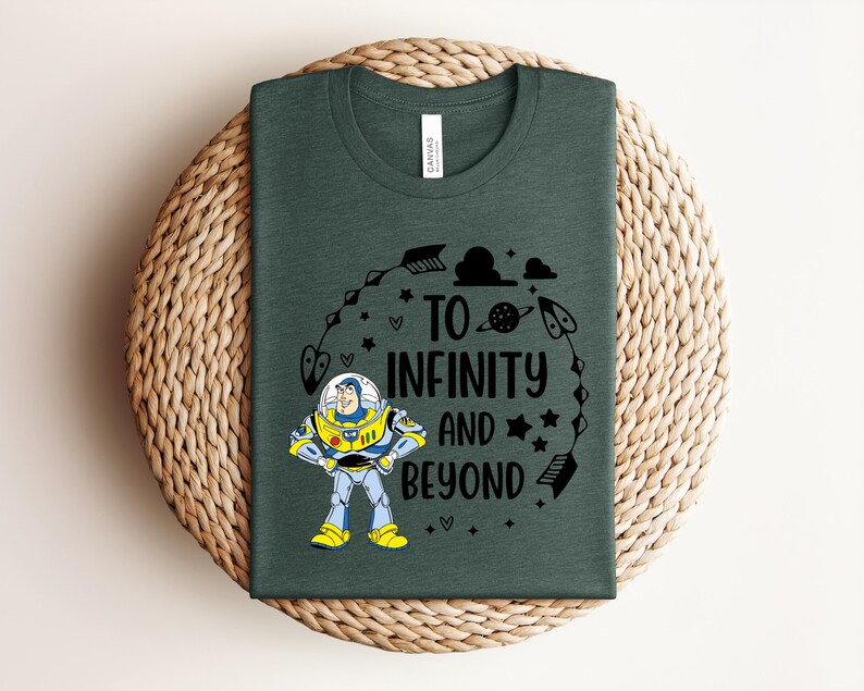 Peut inclure: T-shirt vert fonc&eacute; avec un dessin anim&eacute; de Buzz l'&Eacute;clair et le texte "TO INFINITY AND BEYOND" en noir. Le motif comprend des &eacute;toiles, des fl&egrave;ches et des plan&egrave;tes. Le t-shirt est pr&eacute;sent&eacute; sur une surface tiss&eacute;e.