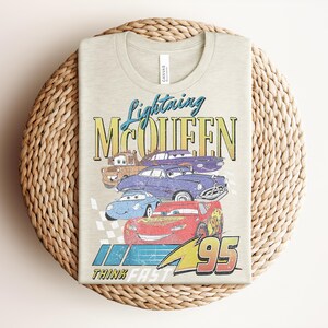 Puede incluir: Camiseta de color beige claro con Lightning McQueen y otros personajes de la pel&iacute;cula Cars. El dise&ntilde;o incluye el texto "Lightning McQueen" y "95", con la frase "Think Fast" debajo.