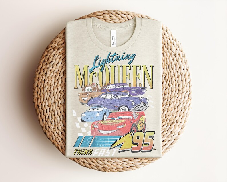 Puede incluir: Camiseta de color beige claro con Lightning McQueen y otros personajes de la pel&iacute;cula Cars. El dise&ntilde;o incluye el texto "Lightning McQueen" y "95", con la frase "Think Fast" debajo.