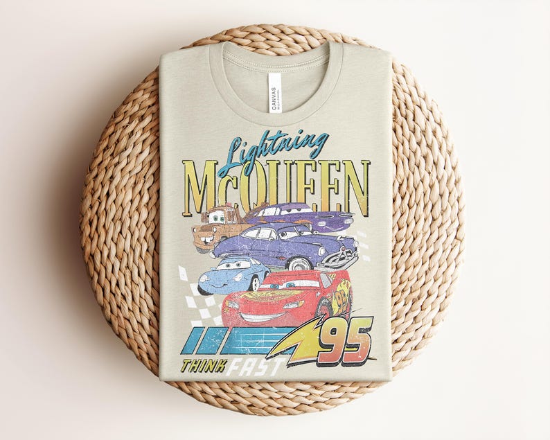 Puede incluir: Una camiseta verde claro con un gr&aacute;fico de Rayo McQueen y otros personajes de Cars. El dise&ntilde;o incluye el texto "Lightning McQueen" y "95", con la frase "Think Fast" debajo. La camiseta est&aacute; doblada sobre una superficie tejida.