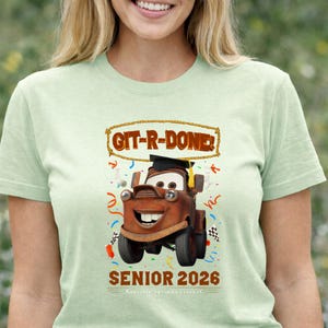 Op de afbeelding: Lichtgroen T-shirt met een cartoonafbeelding van Takel uit de film Cars, met een afstudeerhoed. Het shirt heeft de tekst "GIT-R-DONE!" en "SENIOR 2026". Confetti en geblokte vlaggen zijn ook in het ontwerp opgenomen.