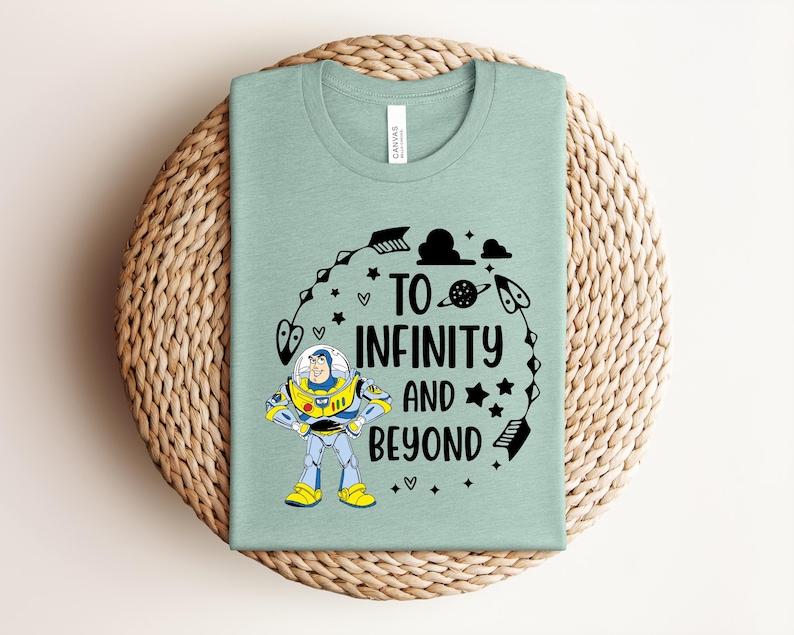 Peut inclure: Un t-shirt vert clair avec le texte "TO INFINITY AND BEYOND" et un dessin anim&eacute; de Buzz l'&Eacute;clair. Le motif comprend des &eacute;toiles, des plan&egrave;tes et des fl&egrave;ches. Le t-shirt est pli&eacute; sur un tapis tiss&eacute;.