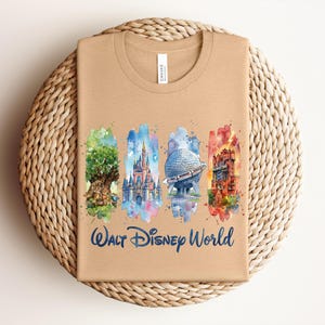 May include: Tan t-shirt featuring watercolor illustrations of iconic Walt Disney World landmarks: the Tree of Life, Cinderella Castle, Spaceship Earth, and the Tower of Terror. The words "Walt Disney World" are written in a blue script font.