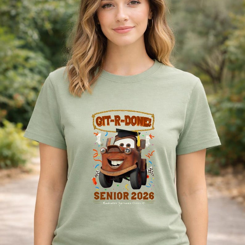 Op de afbeelding: Saliegroen T-shirt met een cartoonafbeelding van Takel uit de film Cars, met een afstudeerhoed. De tekst "GIT-R-DONE!" staat boven Takel en "SENIOR 2026" eronder. Het shirt heeft een ronde hals.