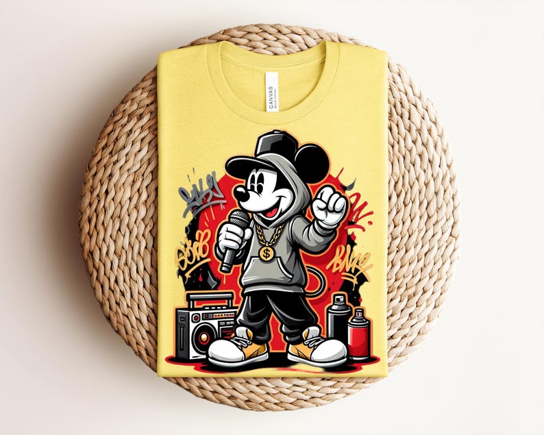 May include: Yellow t-shirt featuring a cartoon illustration of Mickey Mouse in a hip-hop style. Mickey is wearing a gray hoodie, black pants, and a gold chain, holding a microphone. The design includes graffiti art and a boombox.