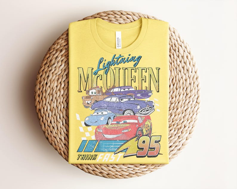 Puede incluir: Camiseta amarilla con un dise&ntilde;o de Rayo McQueen y otros personajes de la pel&iacute;cula Cars. El dise&ntilde;o incluye el texto "Lightning McQueen" y "95", con una bandera a cuadros y las palabras "Think Fast".