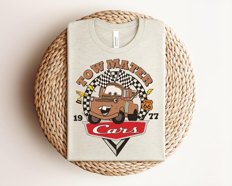 Puede incluir: Una camiseta de color beige claro con un estampado gr&aacute;fico del personaje Tow Mater de la pel&iacute;cula Cars. El dise&ntilde;o incluye una bandera a cuadros, un trofeo dorado, una se&ntilde;al de la Ruta 66, el texto Tow Mater, 1977 y el logo rojo Cars.