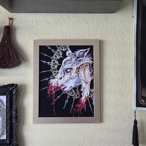 May include: A rectangular framed art print featuring a detailed illustration of a wolf skull with exposed muscle and dripping red blood against a black background. The artwork includes intricate gold filigree patterns radiating from the skull.