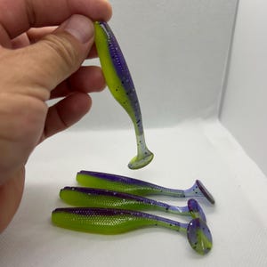 May include: A collection of soft plastic fishing lures. The lures are a vibrant combination of yellow, purple, and green. The lures are designed to mimic small fish, with a paddle tail for movement in the water.