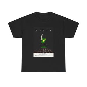 Könnte beinhalten: Ein schwarzes Kurzarm-T-Shirt mit einem grafischen Druck des Alien-Filmplakats. Das Design zeigt ein aufgebrochenes Ei, das grünes Licht ausstrahlt, den Schriftzug ALIEN in weißem Text und kleine Details im unteren Bereich der Grafik.