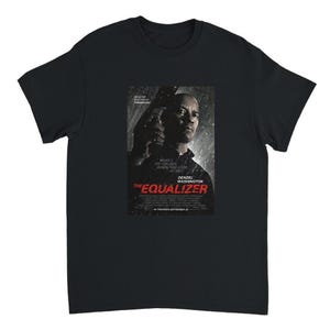 May include: A black short-sleeved t-shirt featuring a graphic print of The Equalizer movie poster. The print displays Denzel Washington holding a firearm, with the text "WHAT DO YOU SEE WHEN YOU LOOK AT ME?" and "THE EQUALIZER" in red lettering.