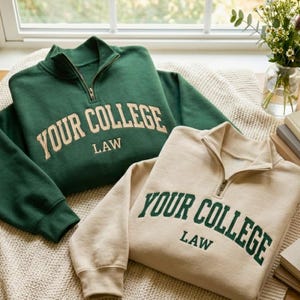 Puede incluir: Dos sudaderas con el texto "YOUR COLLEGE LAW". Una es verde oscuro con texto color crema, y la otra es beige con texto verde. Ambas tienen cuello con cremallera.