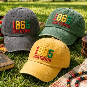 Op de afbeelding: Drie baseballpetten in antracietgrijs, olijfgroen en mosterdgeel. Elke pet is voorzien van geborduurde tekst 1865 in rood, geel en groen, met het woord JUNETEENTH in het rood geborduurd onder de cijfers op het voorpaneel.